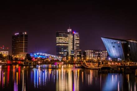 Reflective night view of Amsterdam's modern skyline by the water.
