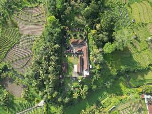 Explore an aerial view of a Balinese temple nestled amidst green rice terraces in Selat, Bali, Indonesia.