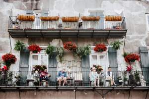 A picturesque New Orleans balcony scene with people relaxing and colorful floral decorations.