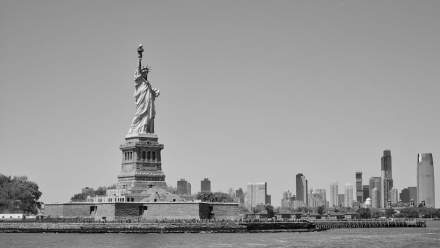 Black and white image of the Statue of Liberty with the New York City skyline.